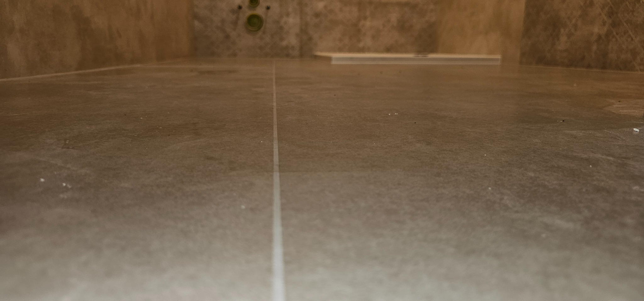 Ułożone szare płytki podłogowe w łazience, widoczne fugi i odpływ liniowy w tle.