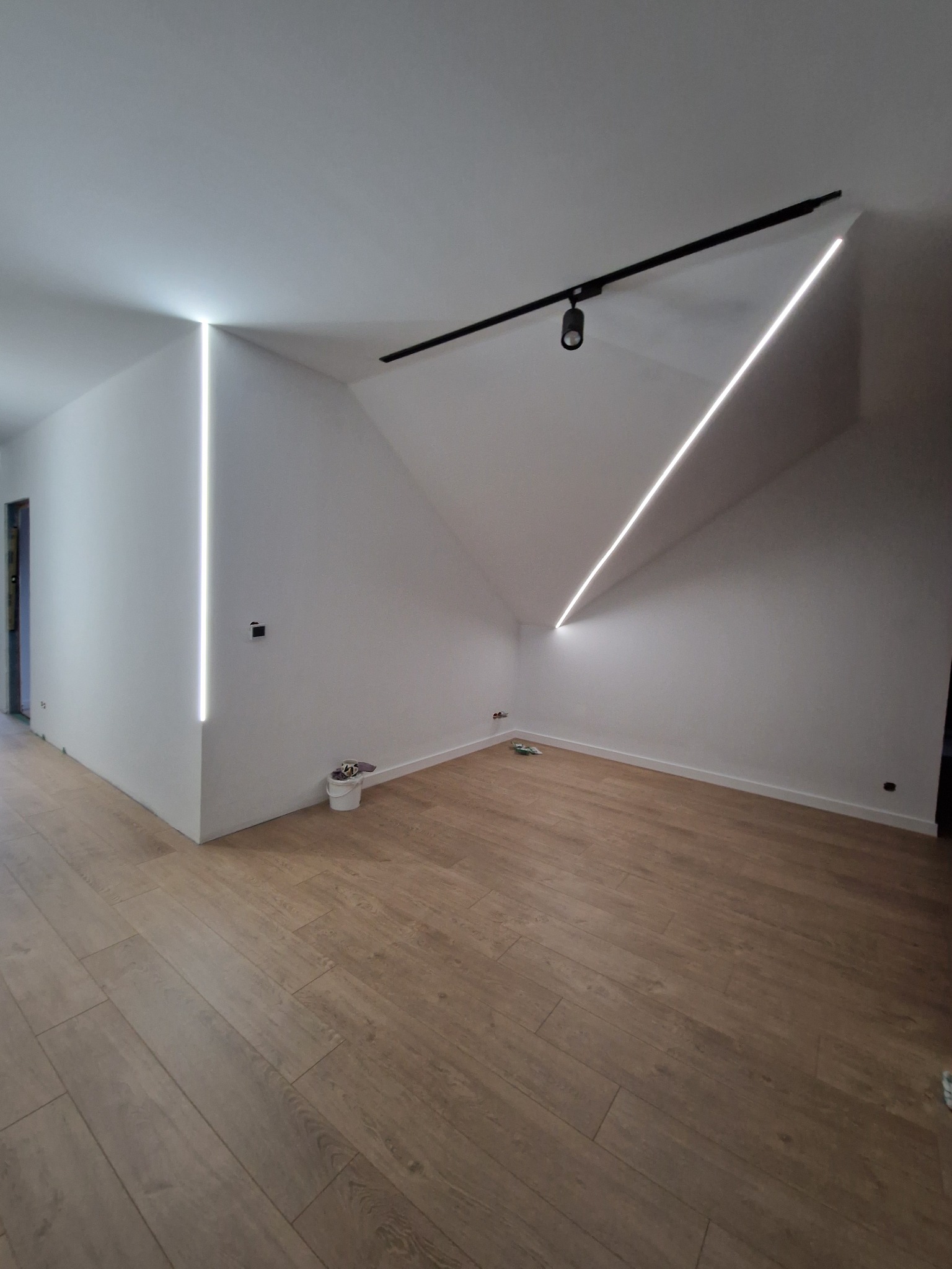 Nowoczesne oświetlenie LED w skosach poddasza, z drewnianą podłogą i czarną szyną oświetleniową.