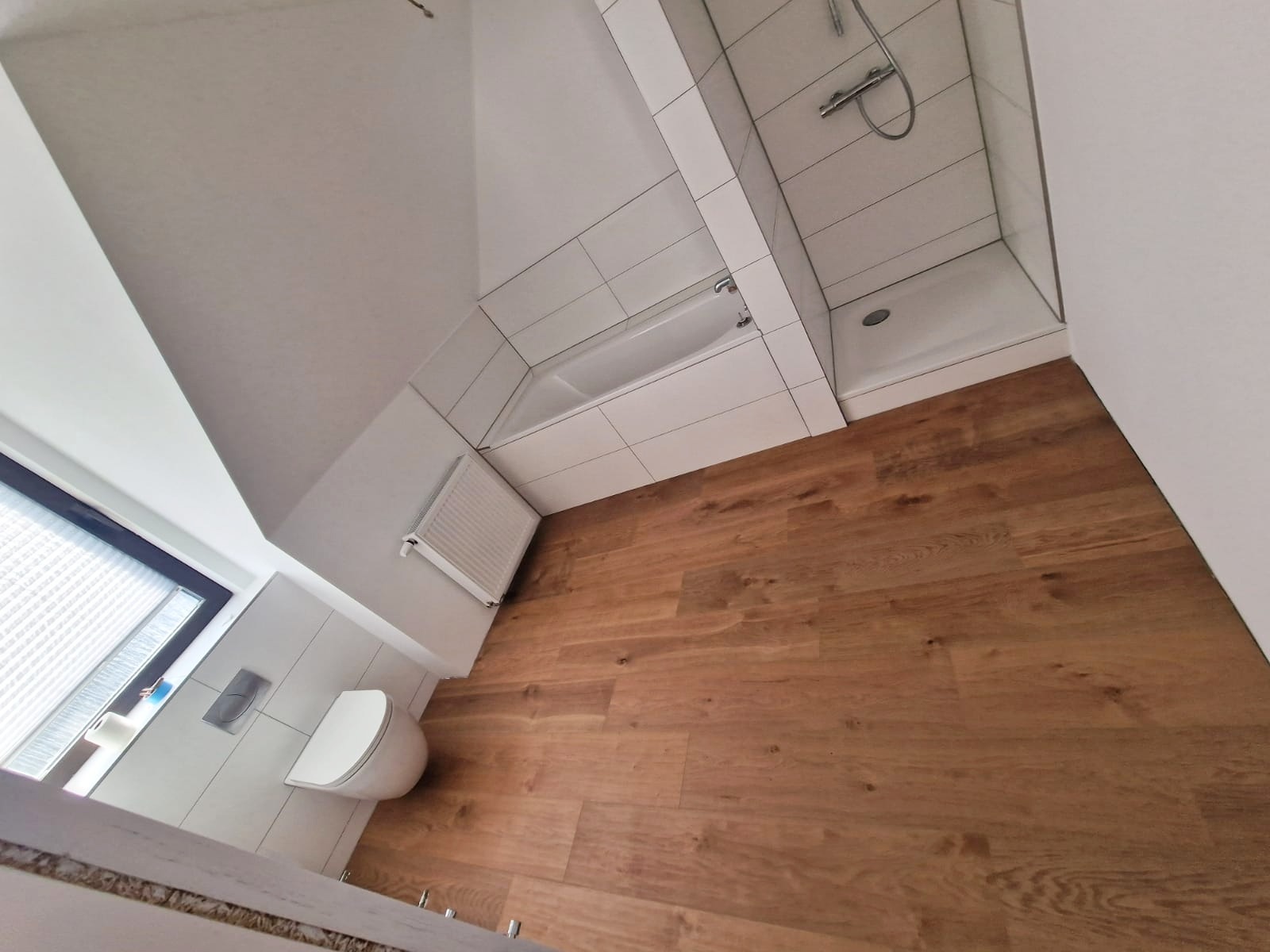 Ukośne ujęcie wykończonej łazienki z drewnopodobną podłogą, białą armaturą, wanną i kabiną prysznicową, widok z góry.