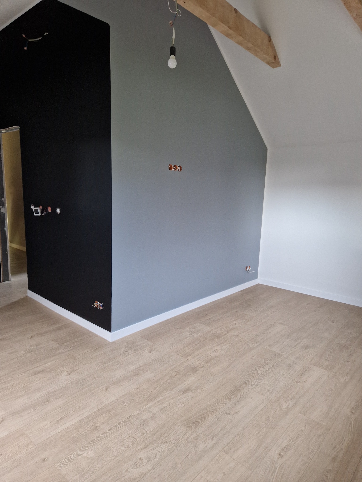 Wnętrze pokoju po malowaniu ścian na czarno, szaro i biało, z drewnianą podłogą i widocznymi instalacjami elektrycznymi bez osprzętu.