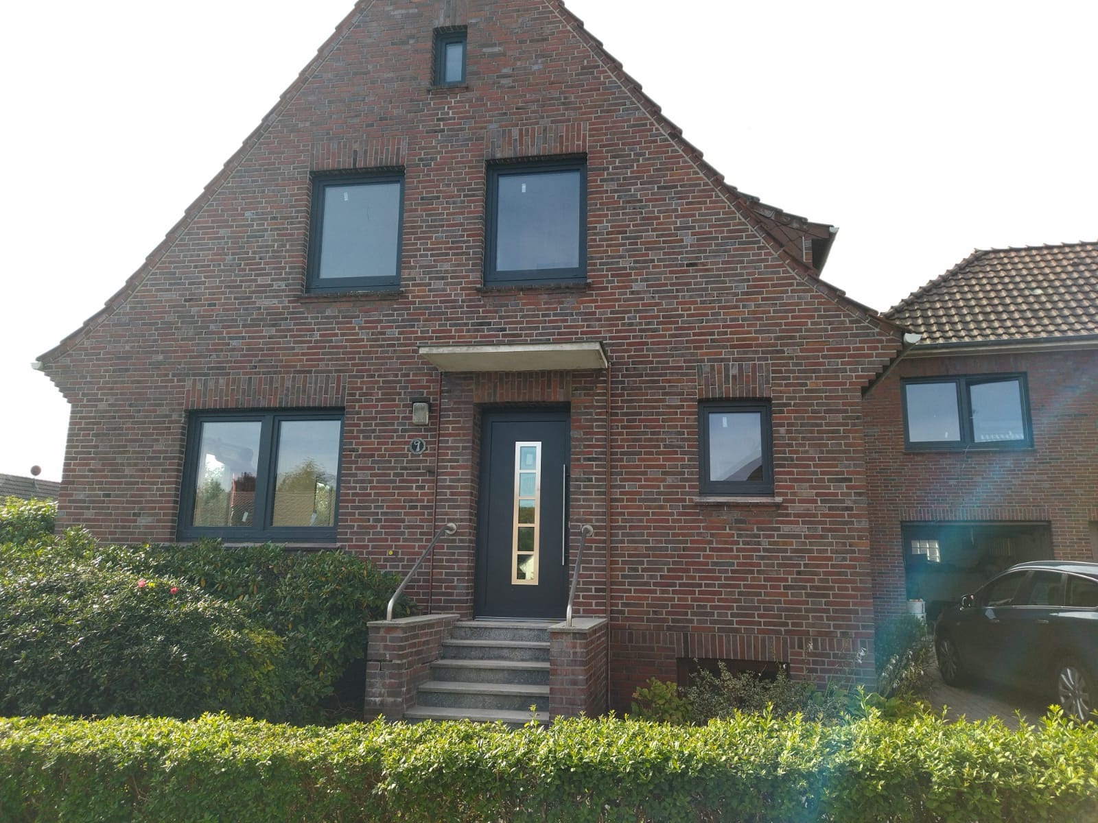 Ceglany dom jednorodzinny z ciemnymi oknami i drzwiami wejściowymi z elementami dekoracyjnymi, widok z poziomu ogrodu.