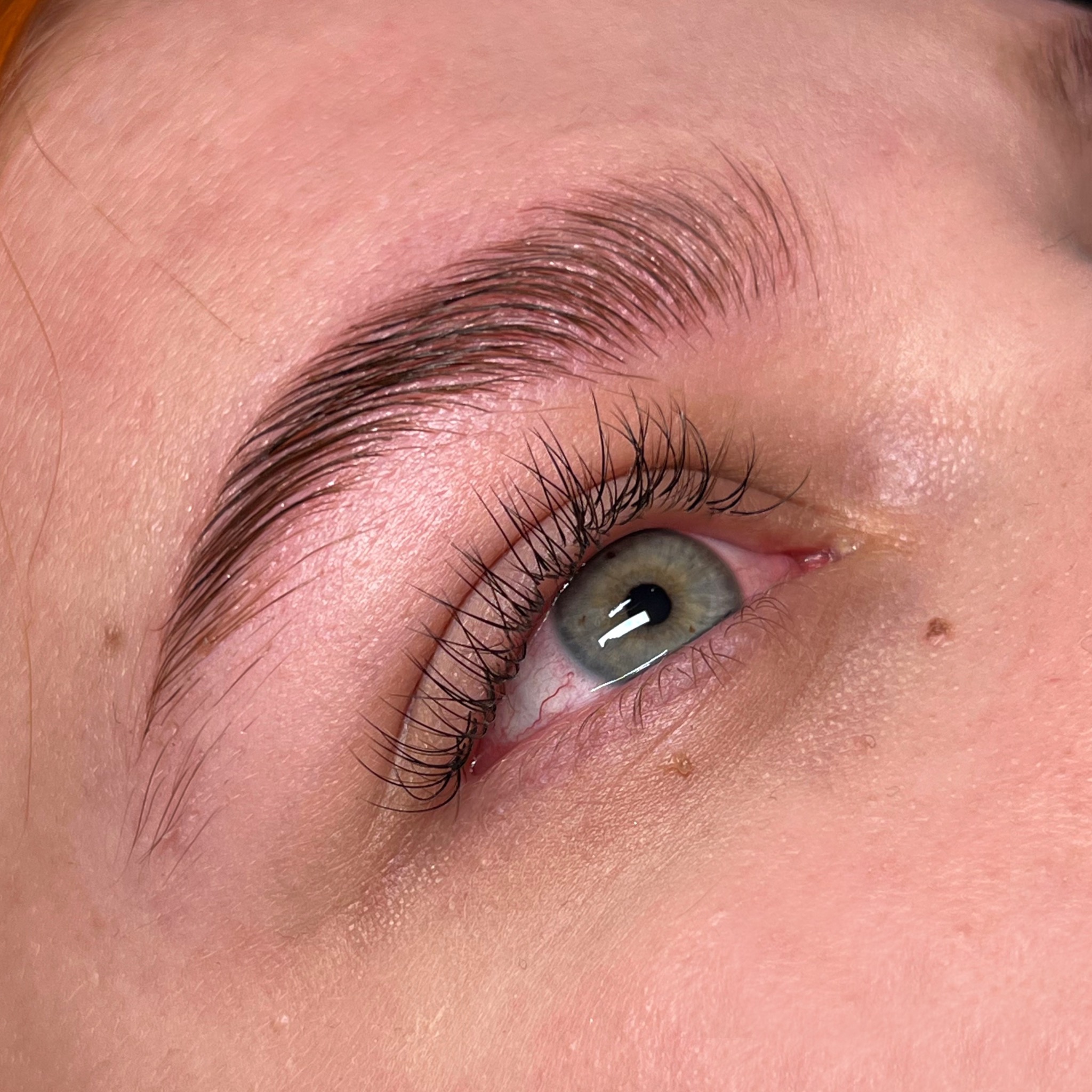 Zbliżenie na oko z brwiami po laminacji i liftingu rzęs, widoczne pojedyncze włoski i zielona tęczówka oka