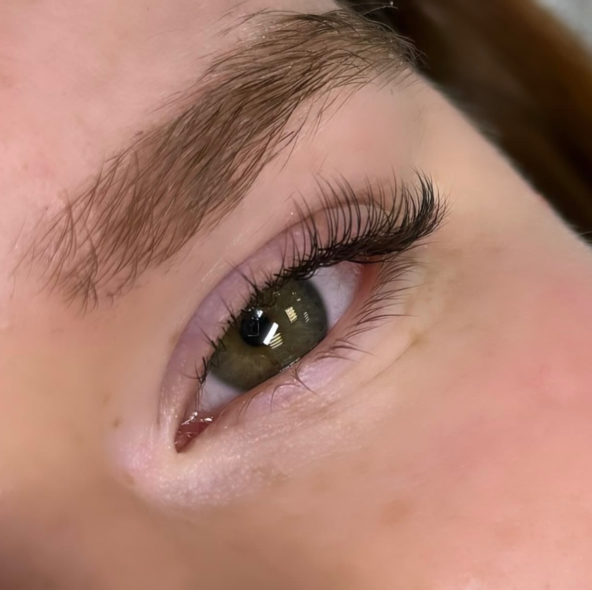 Zbliżenie na oko z przedłużonymi, gęstymi, czarnymi rzęsami; widoczny delikatny makijaż oka i naturalna brew.