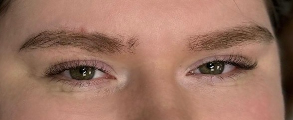 Zbliżenie na parę zielonych oczu z przedłużonymi rzęsami, widoczne brwi o naturalnym wyglądzie i delikatny makijaż oka w odcieniach różu.