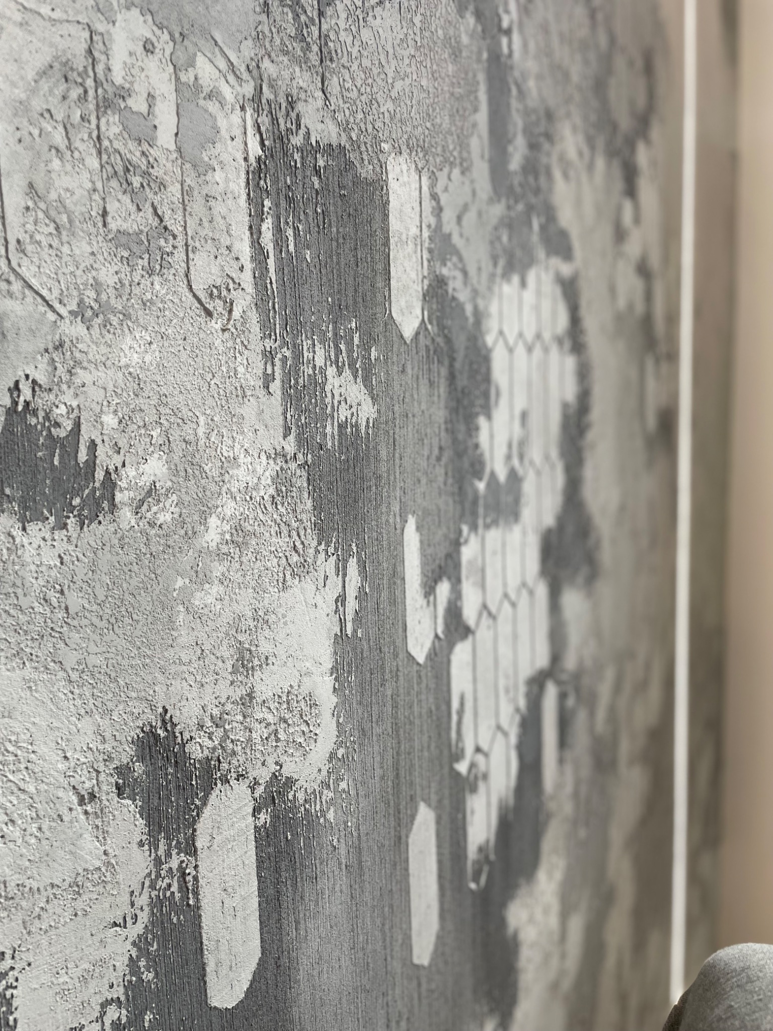 Szara ściana z efektem dekoracyjnym, imitującym surowy beton i fragment wzoru heksagonalnego, wykonana techniką strukturalną.