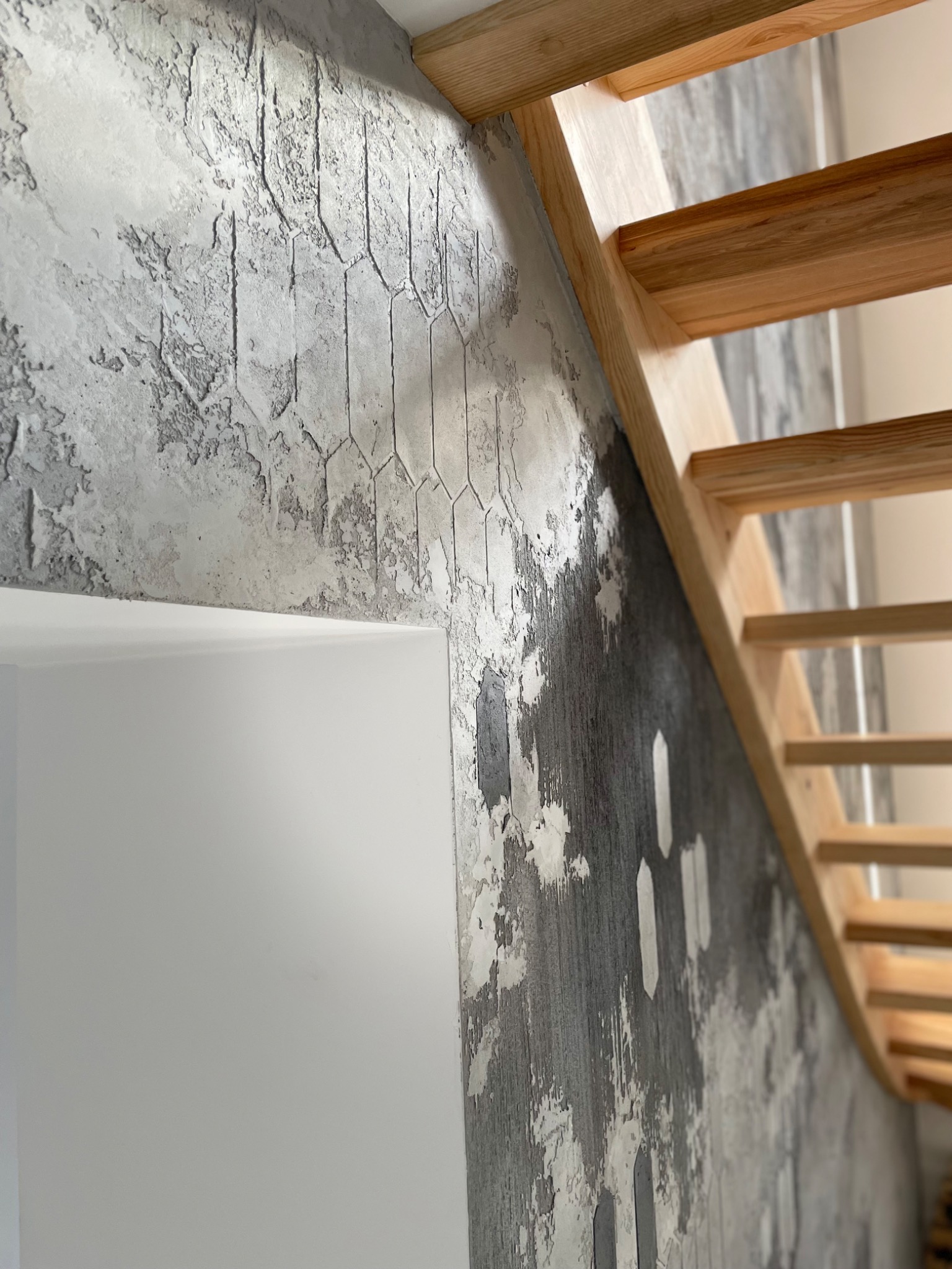 Ściana z dekoracyjnym tynkiem imitującym beton z geometrycznym wzorem obok drewnianych schodów.