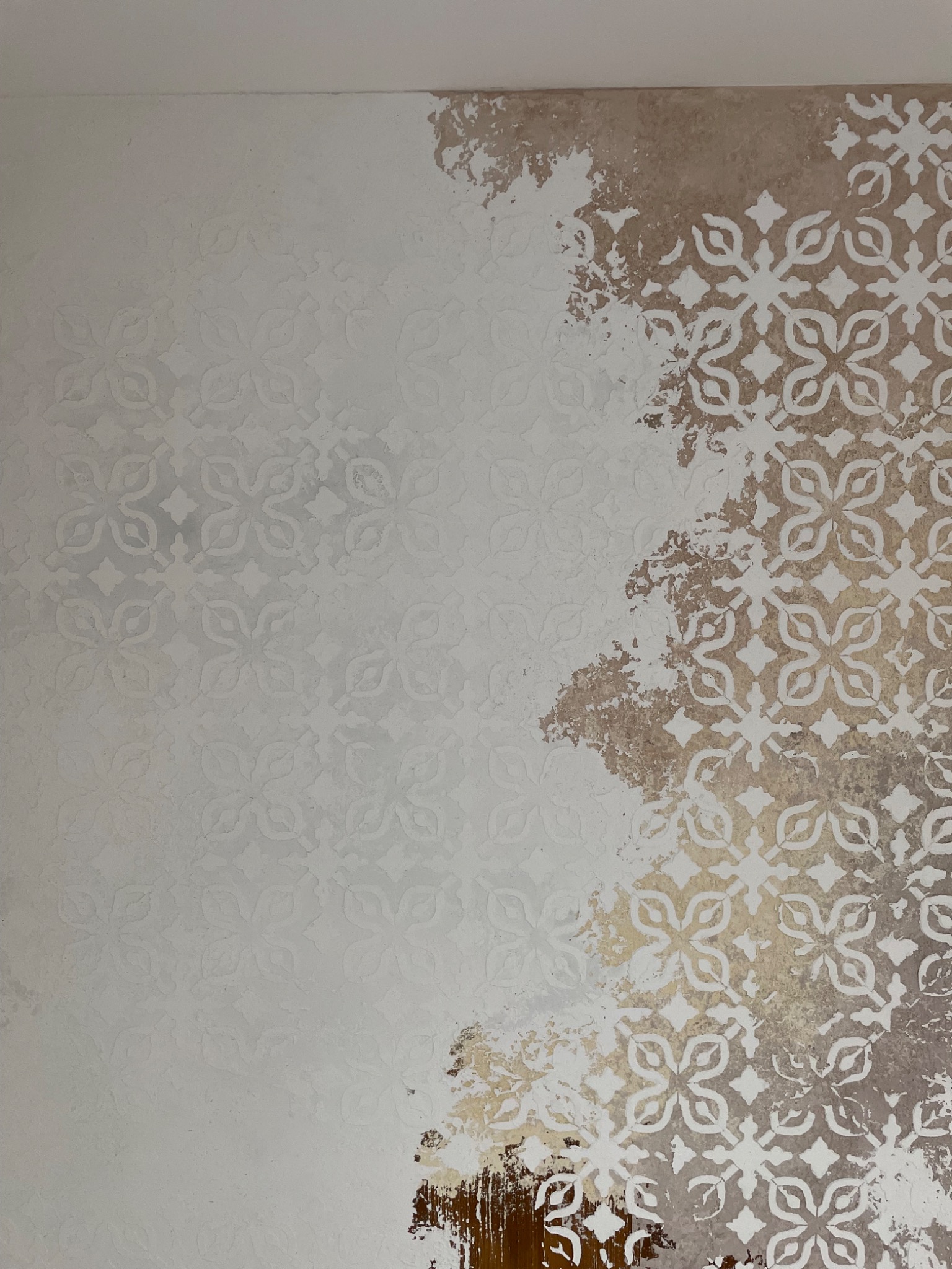 Ściana z dekoracyjnym wzorem kwiatowym, częściowo pokryta złotobrązową farbą, tworząc efekt postarzenia i niedokończenia.