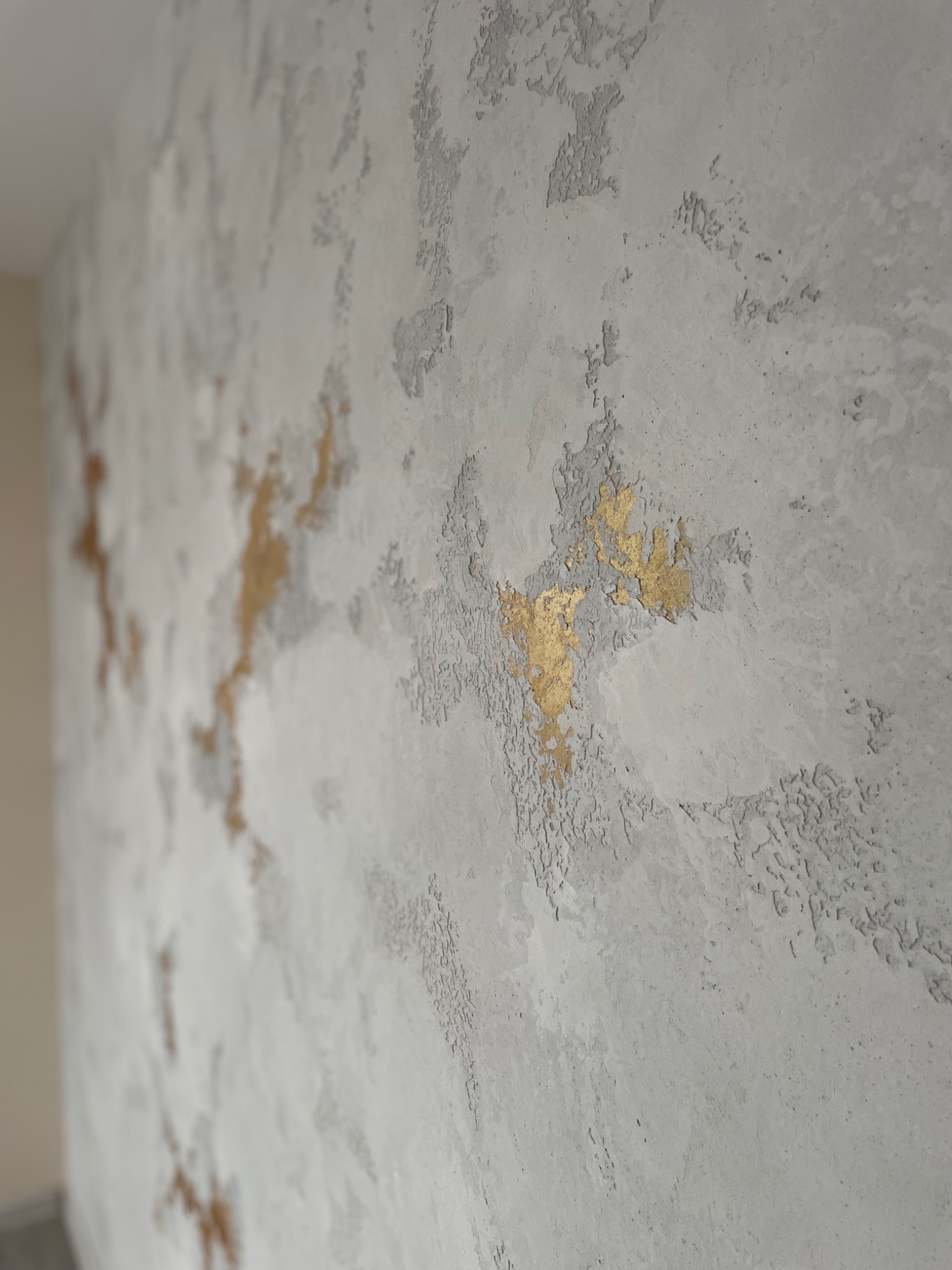 Szara ściana z efektem betonu i złotymi akcentami, dekoracyjna faktura z bliska.