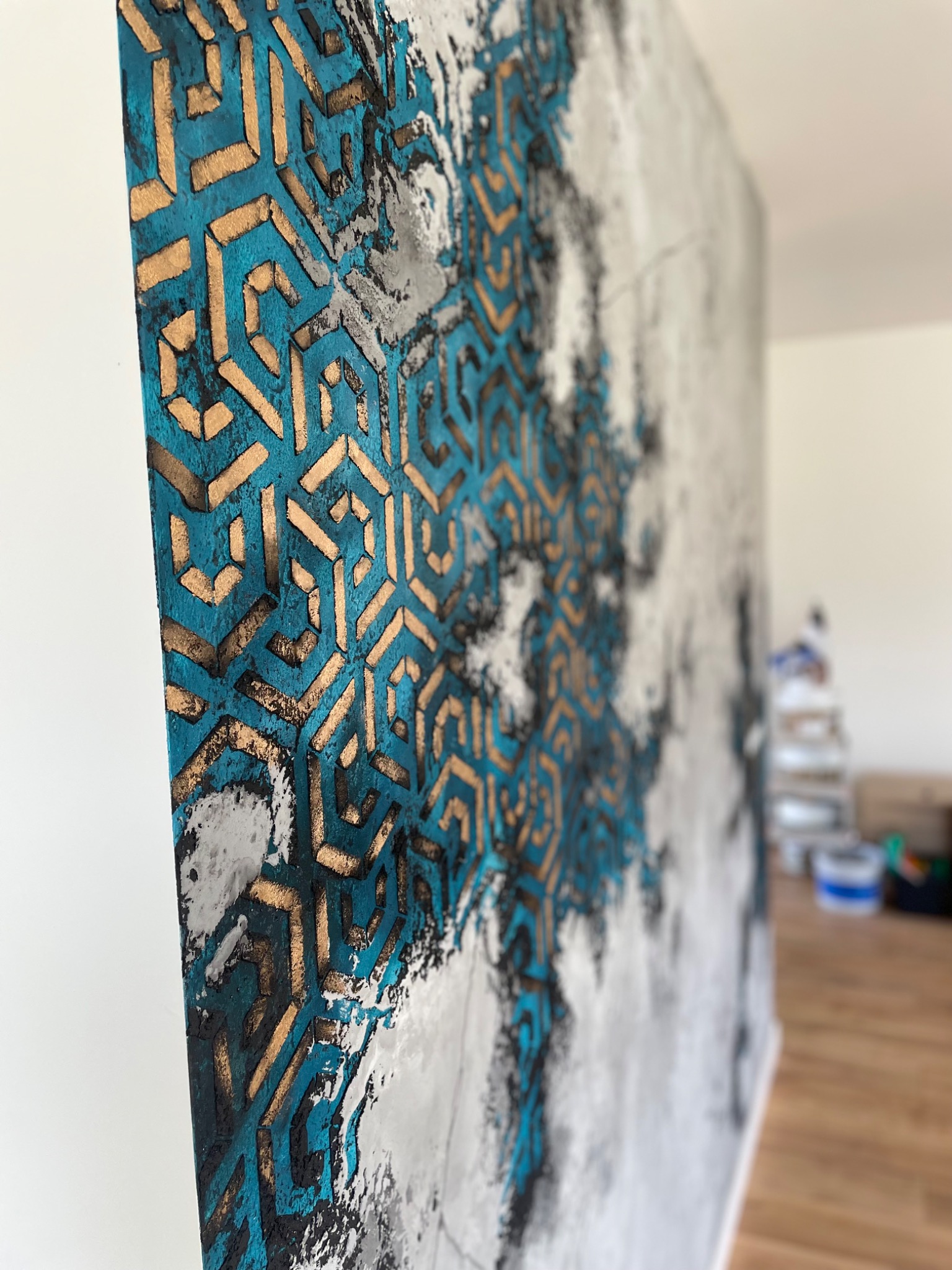 Ściana z artystycznym wzorem w odcieniach błękitu, złota i szarości, wykonanym w Kędzierzynie-Koźlu. Geometryczny motyw z efektem trójwymiarowości.