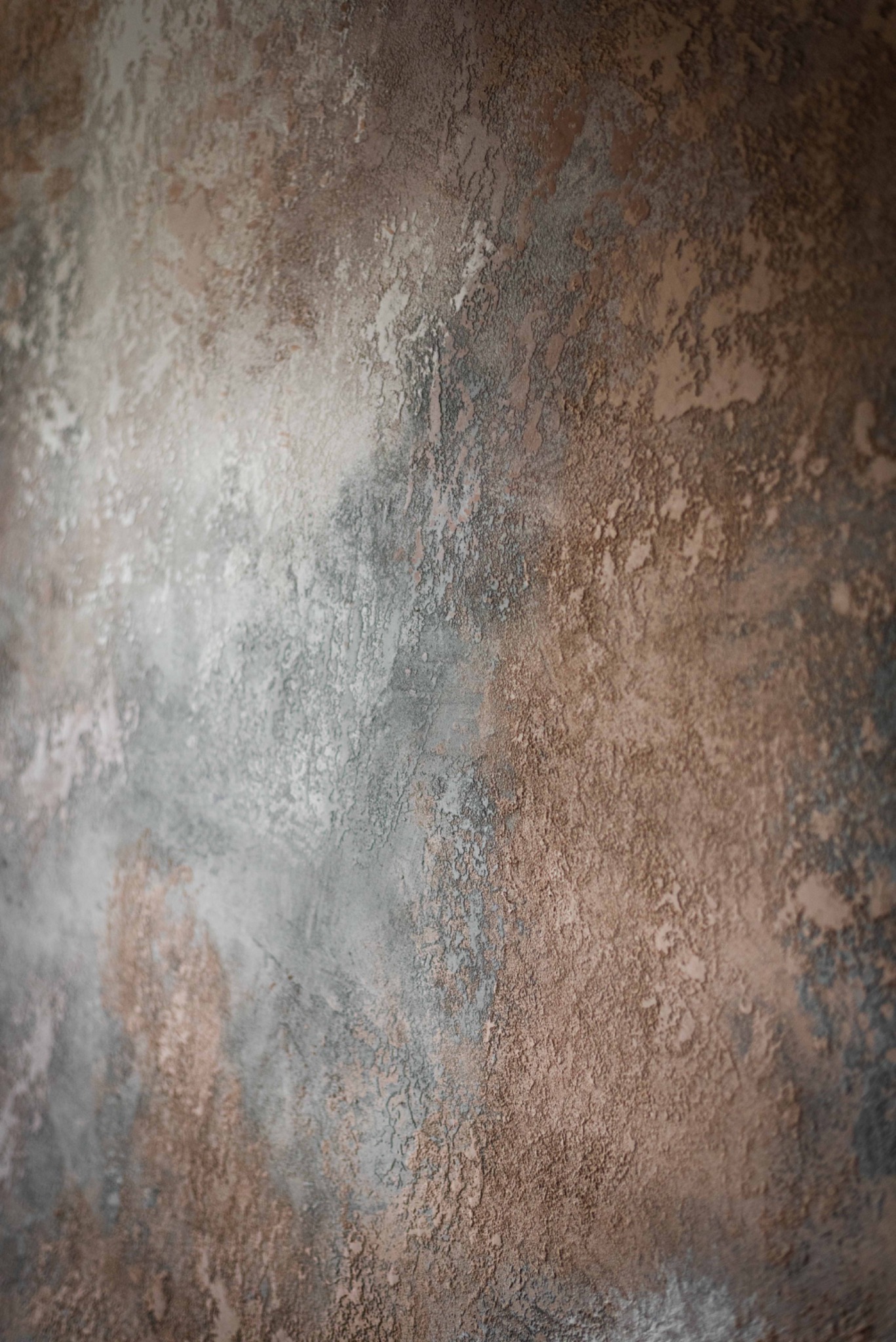 Dekoracyjna ściana z efektem betonu w odcieniach szarości, brązu i beżu, z wyraźną fakturą i nierównomiernym rozłożeniem kolorów, tworząca unikalny wzór.