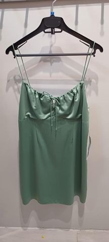 Jasnozielona, satynowa sukienka na ramiączkach, wisząca na czarnym wieszaku na tle jasnej ściany. Dekolt marszczony ze sznurkiem do wiązania.