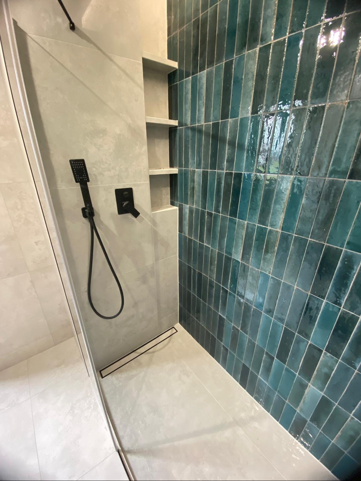 Nowoczesna kabina prysznicowa z turkusową glazurą ułożoną pionowo, czarną armaturą i wnękami w ścianie. Minimalistyczny design.