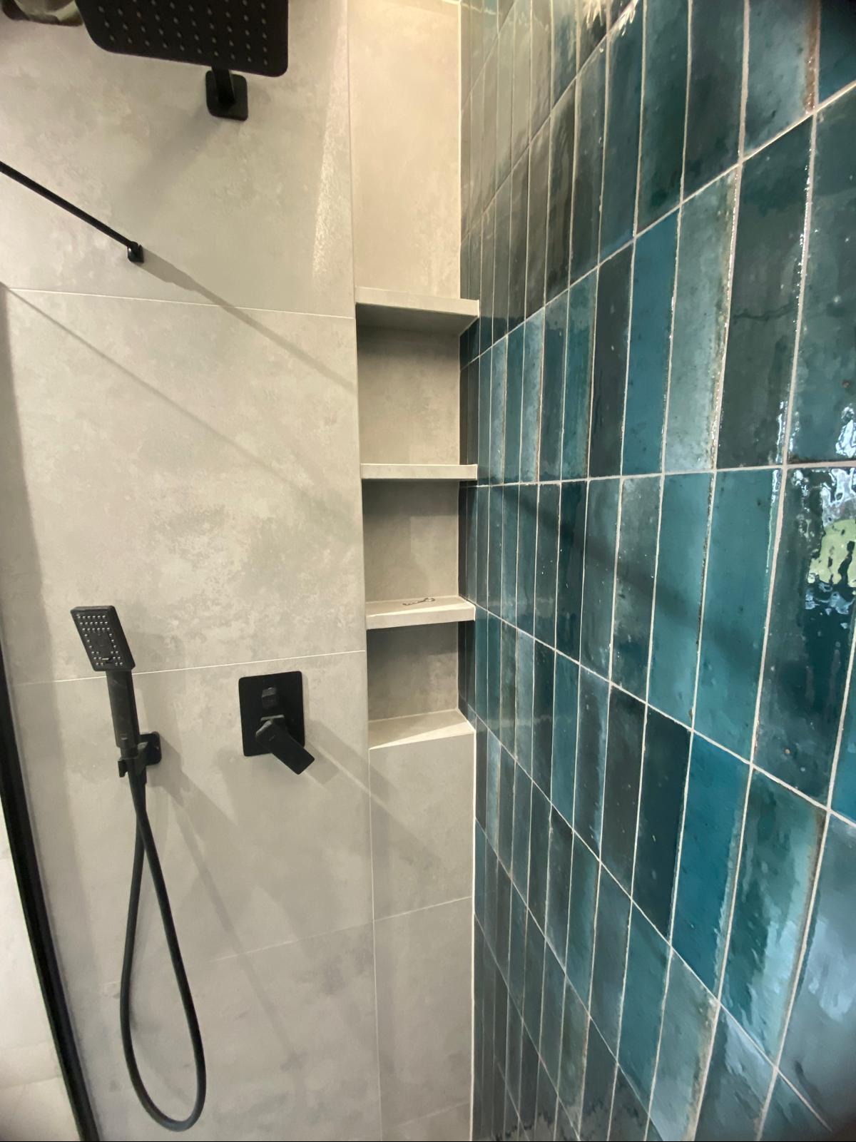 Nowoczesna kabina prysznicowa z turkusową, pionową glazurą, szarą ścianą z wnękami i czarną armaturą. Minimalistyczny design z kontrastującymi kolorami i fakturami.