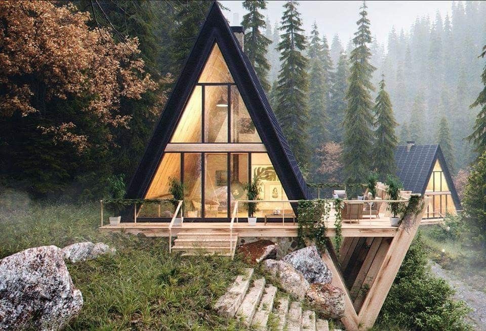 Nowoczesny, trójkątny dom z dużymi przeszkleniami, usytuowany na zboczu w otoczeniu lasu iglastego, z drewnianym tarasem i schodami prowadzącymi do wejścia.