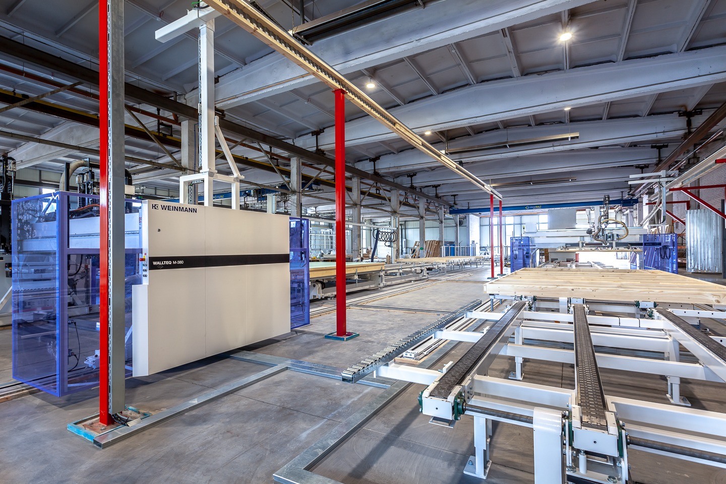 Wnętrze hali produkcyjnej z maszyną CNC Weinmann Wallteq M-380 do obróbki drewna i elementami konstrukcyjnymi w trakcie montażu na linii produkcyjnej.