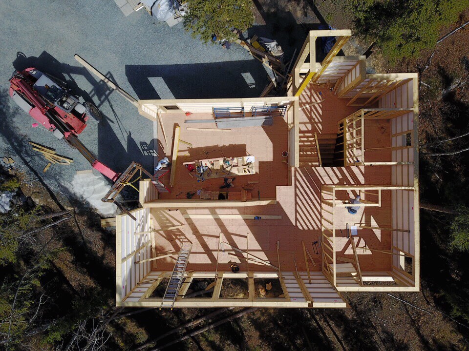Widok z lotu ptaka na budowę domu z drewnianą konstrukcją szkieletową, z widocznym dźwigiem i elementami konstrukcyjnymi wewnątrz.