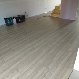 Volodymyr Rokush - Beżowe panele ułożone w skos na poddaszu, widoczny fragment schodów w trakcie budowy i narzędzia pracy przy ścianie.