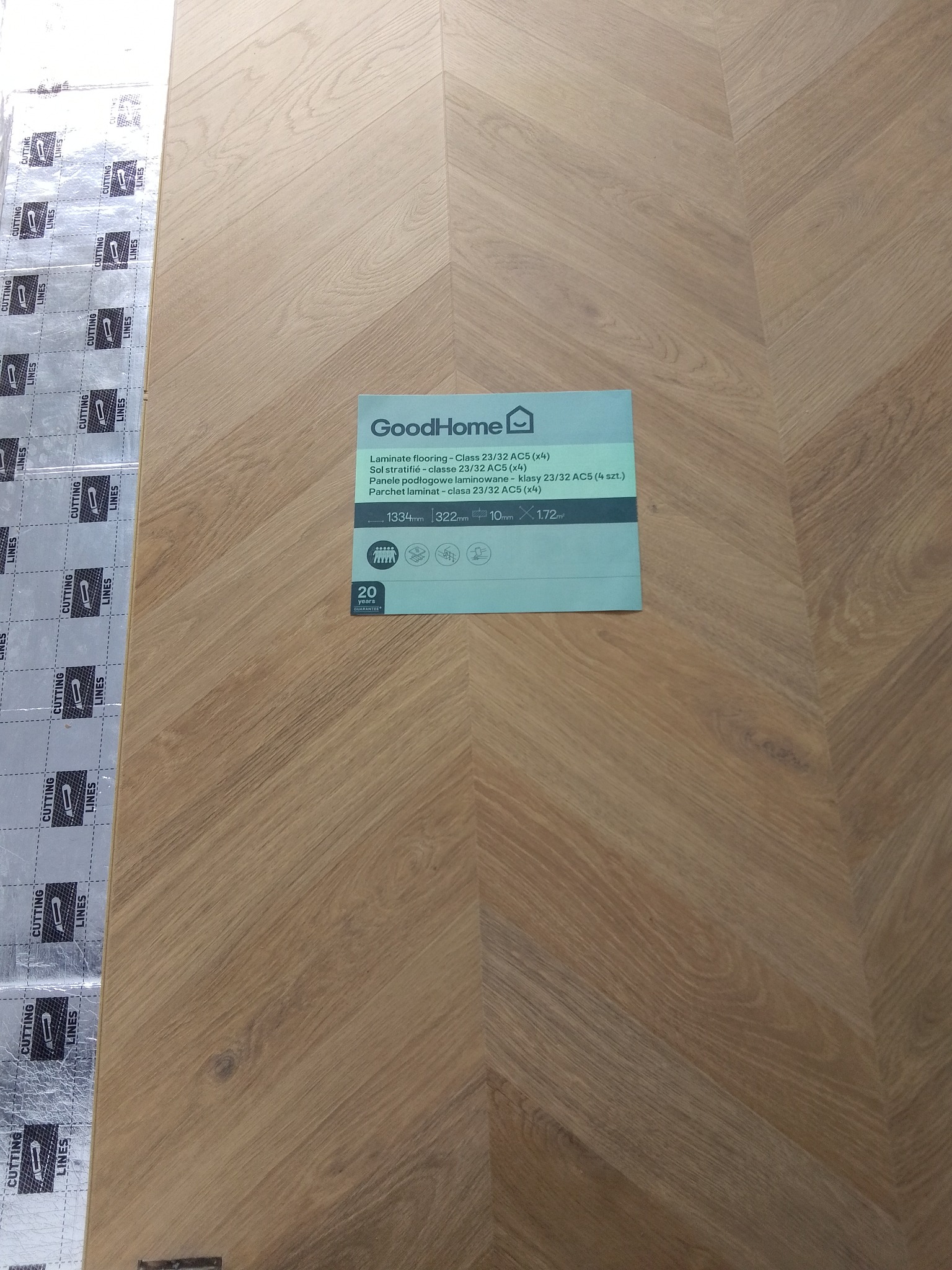 Panele laminowane GoodHome w jodełkę, z widoczną podkładką izolacyjną i etykietą produktu.