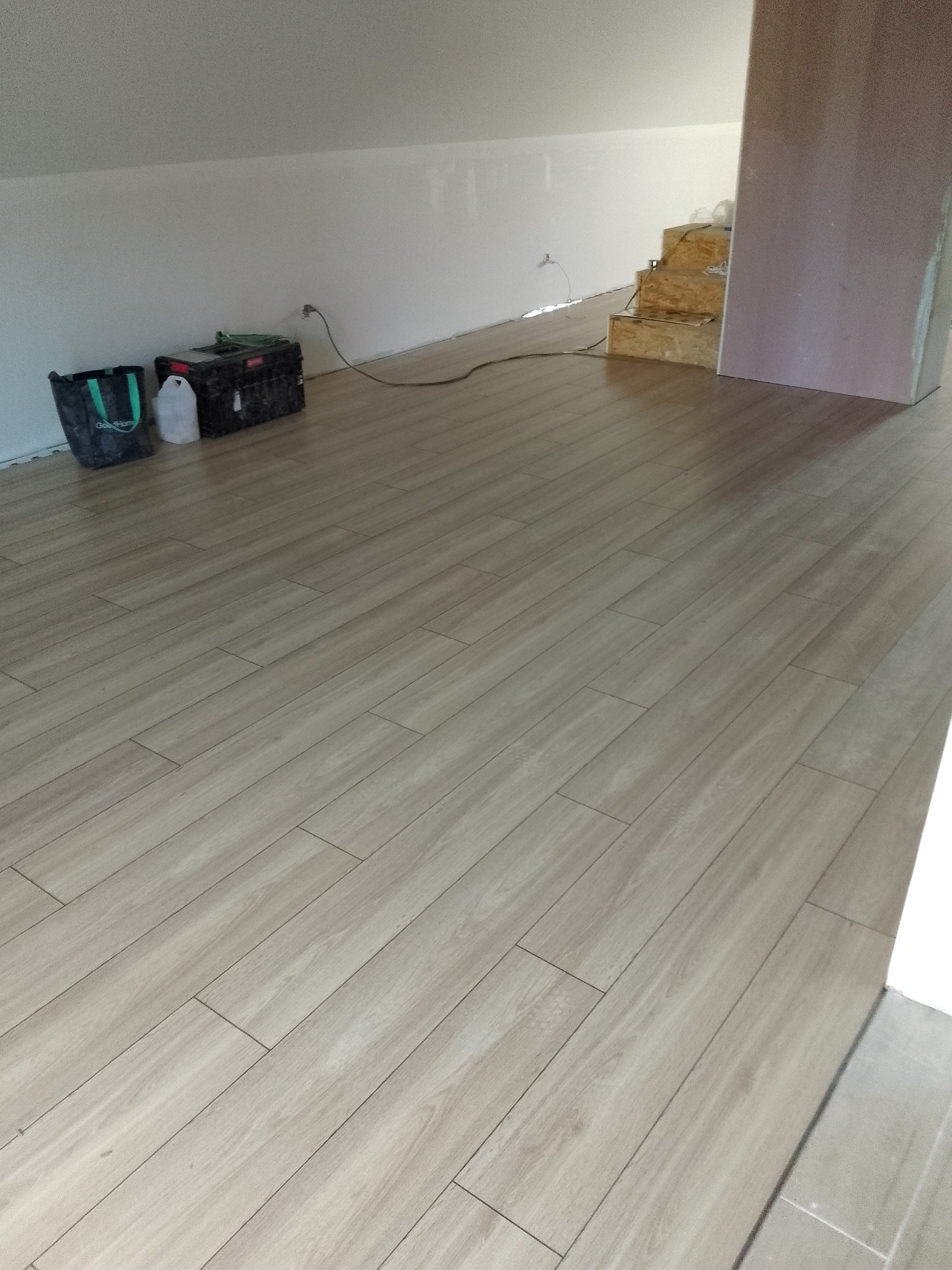 Beżowe panele ułożone w skos na poddaszu, widoczny fragment schodów w trakcie budowy i narzędzia pracy przy ścianie.