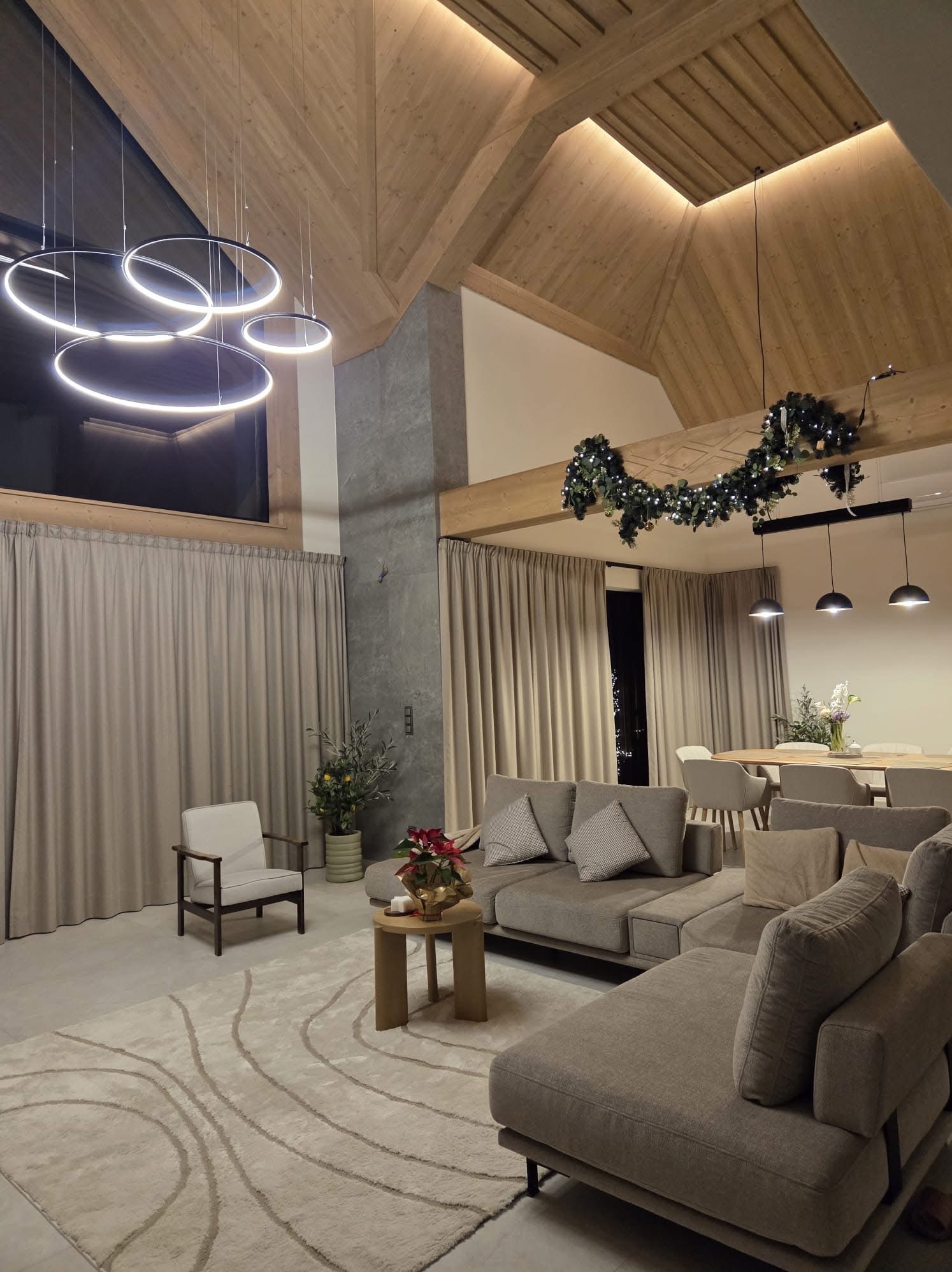 Nowoczesny salon z drewnianym stropem i okrągłymi lampami LED. Dekoracje świąteczne dodają przytulności. Widoczne elementy oświetlenia podsufitowego.