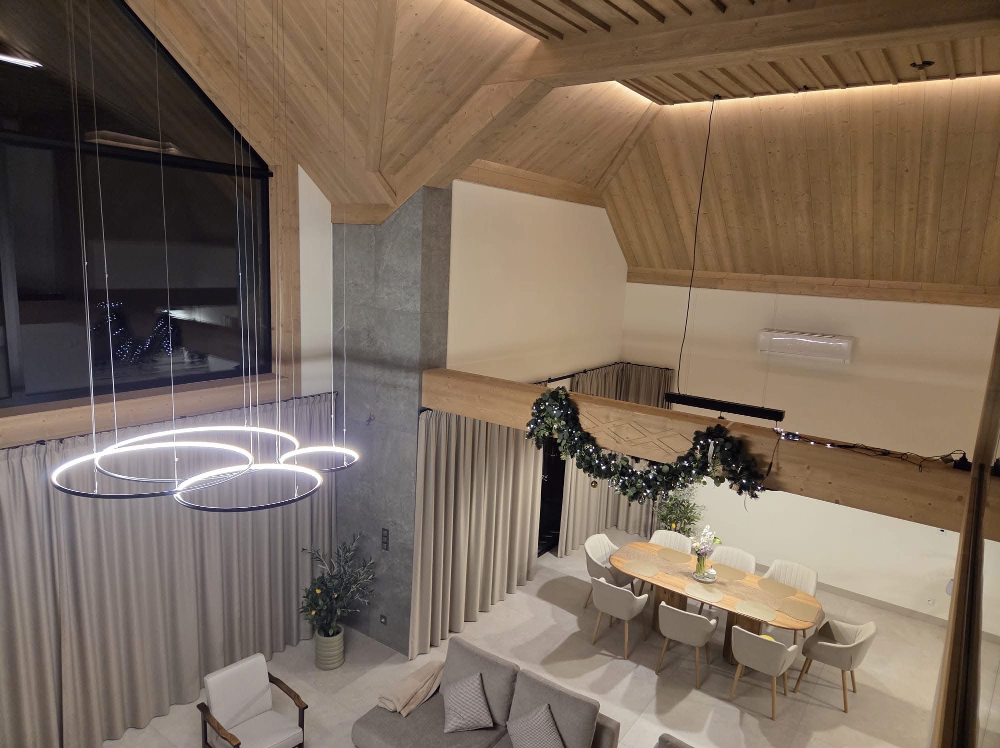 Nowoczesny salon z drewnianą konstrukcją stropu, oświetleniem LED i dekoracjami świątecznymi. Widok z góry na strefę wypoczynkową i jadalnię w przestronnym wnętrzu.
