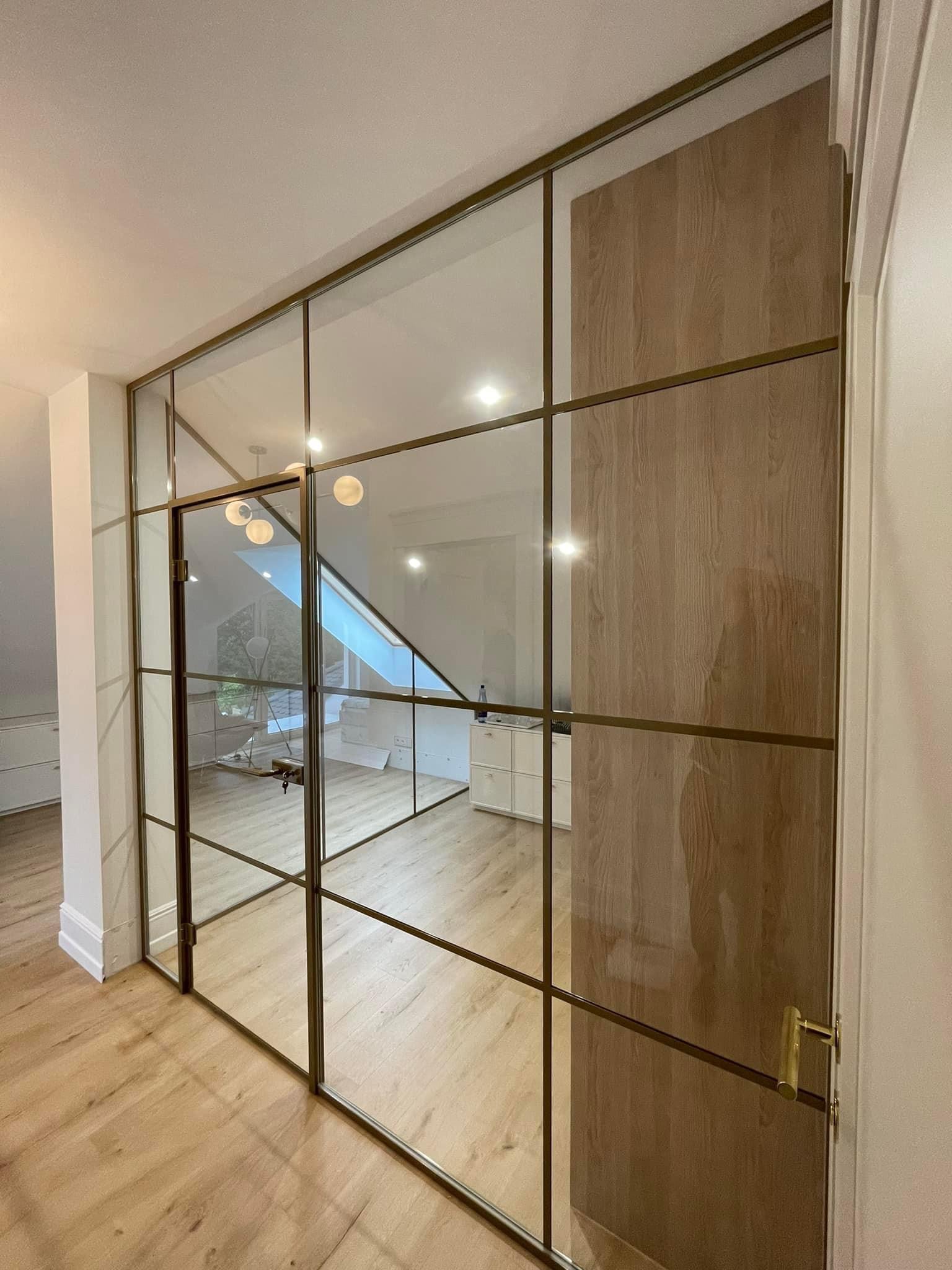 Przeszklona ściana działowa z drewnianymi elementami i drzwiami, widok na skosy poddasza i minimalistyczne wnętrze.