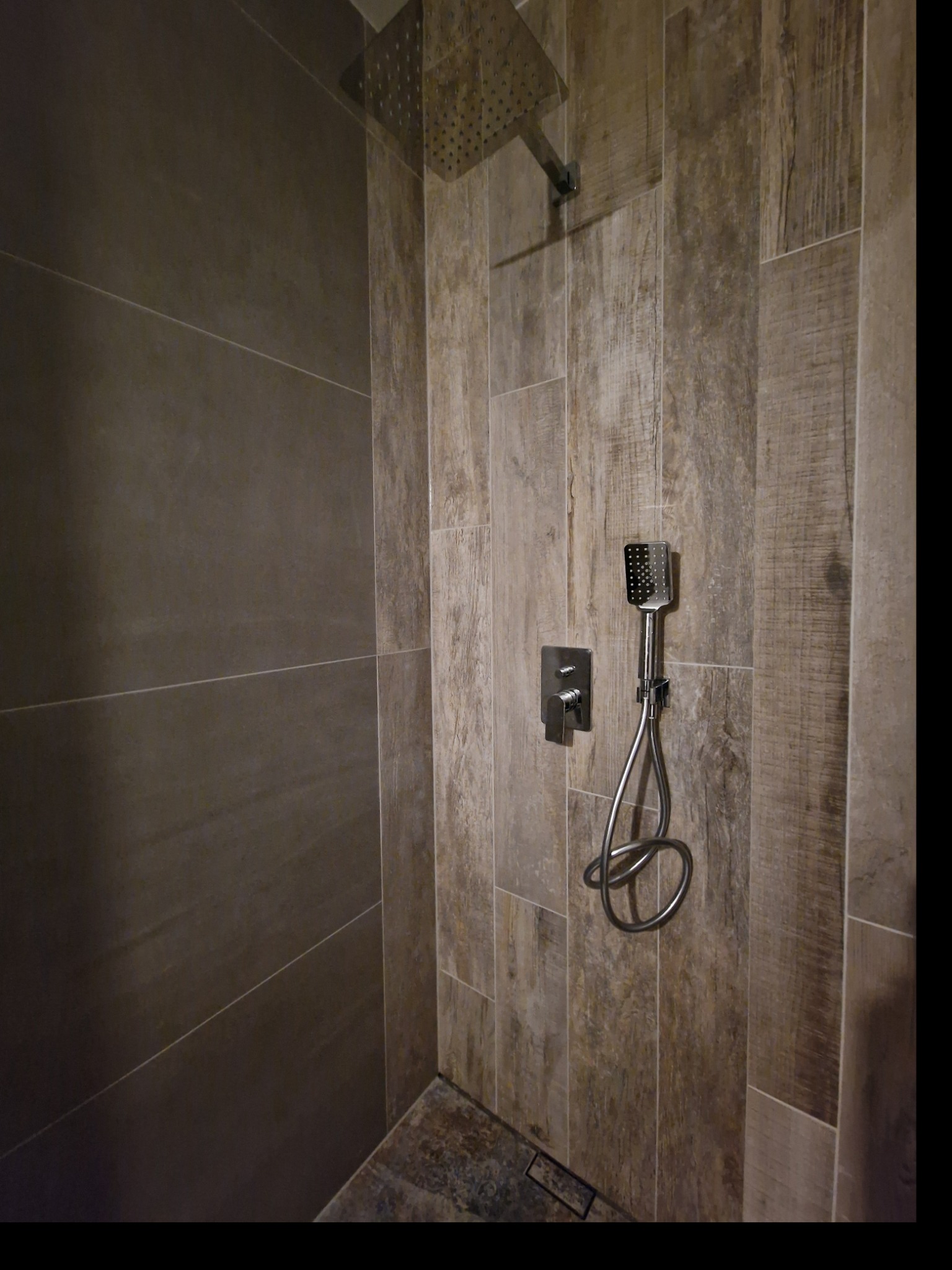 Nowoczesna kabina prysznicowa z deszczownicą i baterią podtynkową, wykończona płytkami imitującymi drewno i szarym gresem.