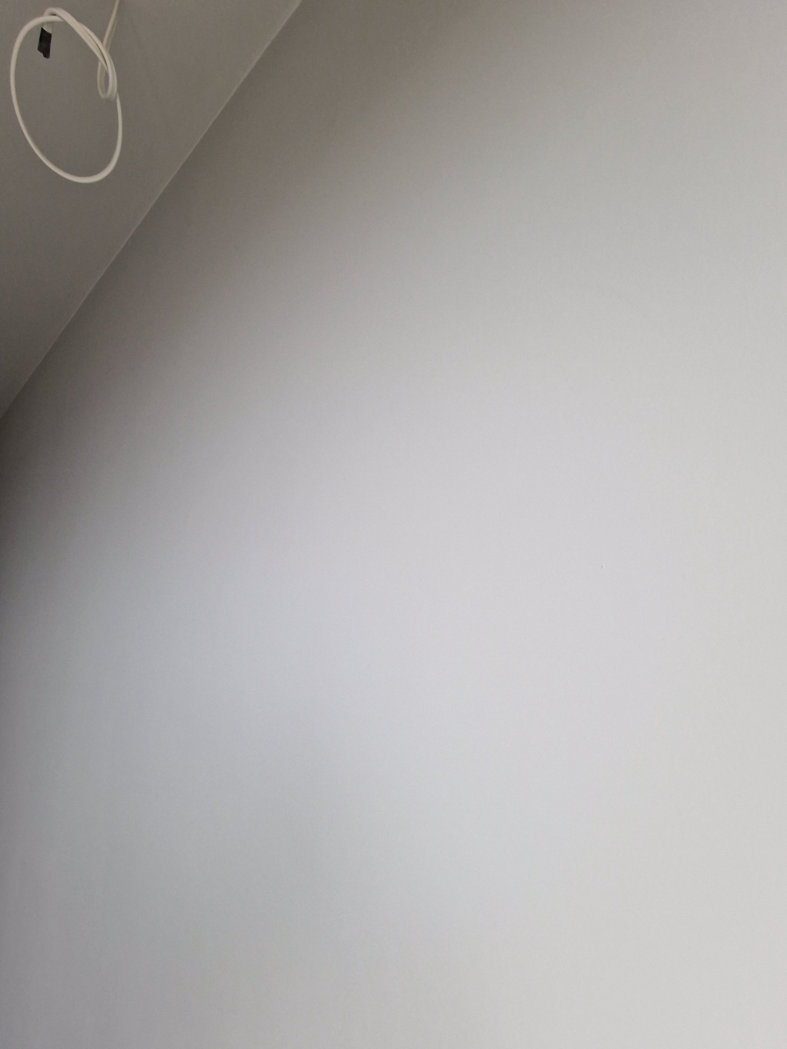 Świeżo pomalowana, gładka ściana w odcieniach szarości, z widocznym fragmentem sufitu i wystającym kablem elektrycznym w rogu.