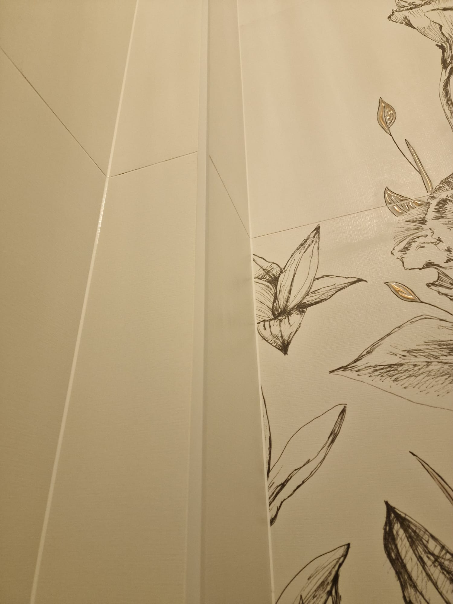 Beżowe płytki ścienne z delikatnym, ręcznie rysowanym motywem kwiatowym w łazience. Widoczne fugi i krawędzie płytek.