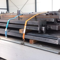 BEDSTALL Marlena Biedra - Stalowe elementy konstrukcyjne, zabezpieczone pasami transportowymi, na platformie pojazdu dostawczego. Widoczne spawy i otwory montażowe.