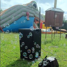 Daria Centka Jendrzej - Maszyna do baniek mydlanych na trawie, w tle dmuchany zamek i drewniana konstrukcja. Sprzęt nagłośnieniowy Tonsil. Atrakcje na imprezę plenerową.