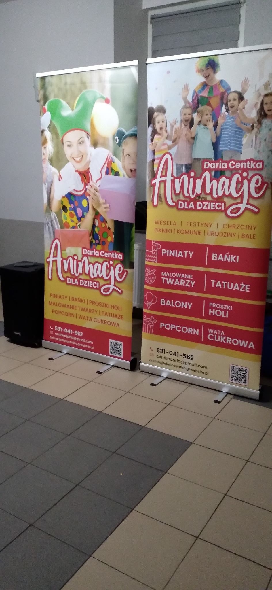 Dwa roll-upy reklamowe z ofertą animacji dla dzieci: klaun, malowanie twarzy, balony, wata cukrowa. Widoczny głośnik. Reklama Daria Centka Animacje dla dzieci.