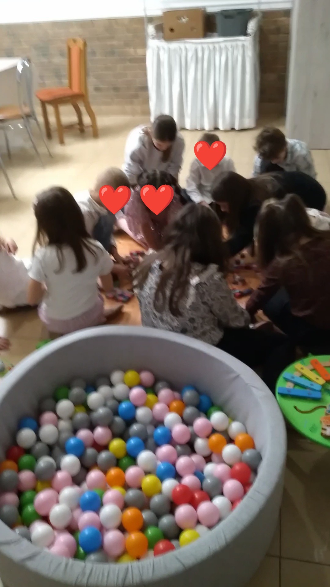 Dzieci bawią się w basenie z kulkami podczas imprezy urodzinowej. Widoczne kolorowe piłeczki i fragmenty dekoracji. Ujęcie z góry, w tle krzesła i stół.