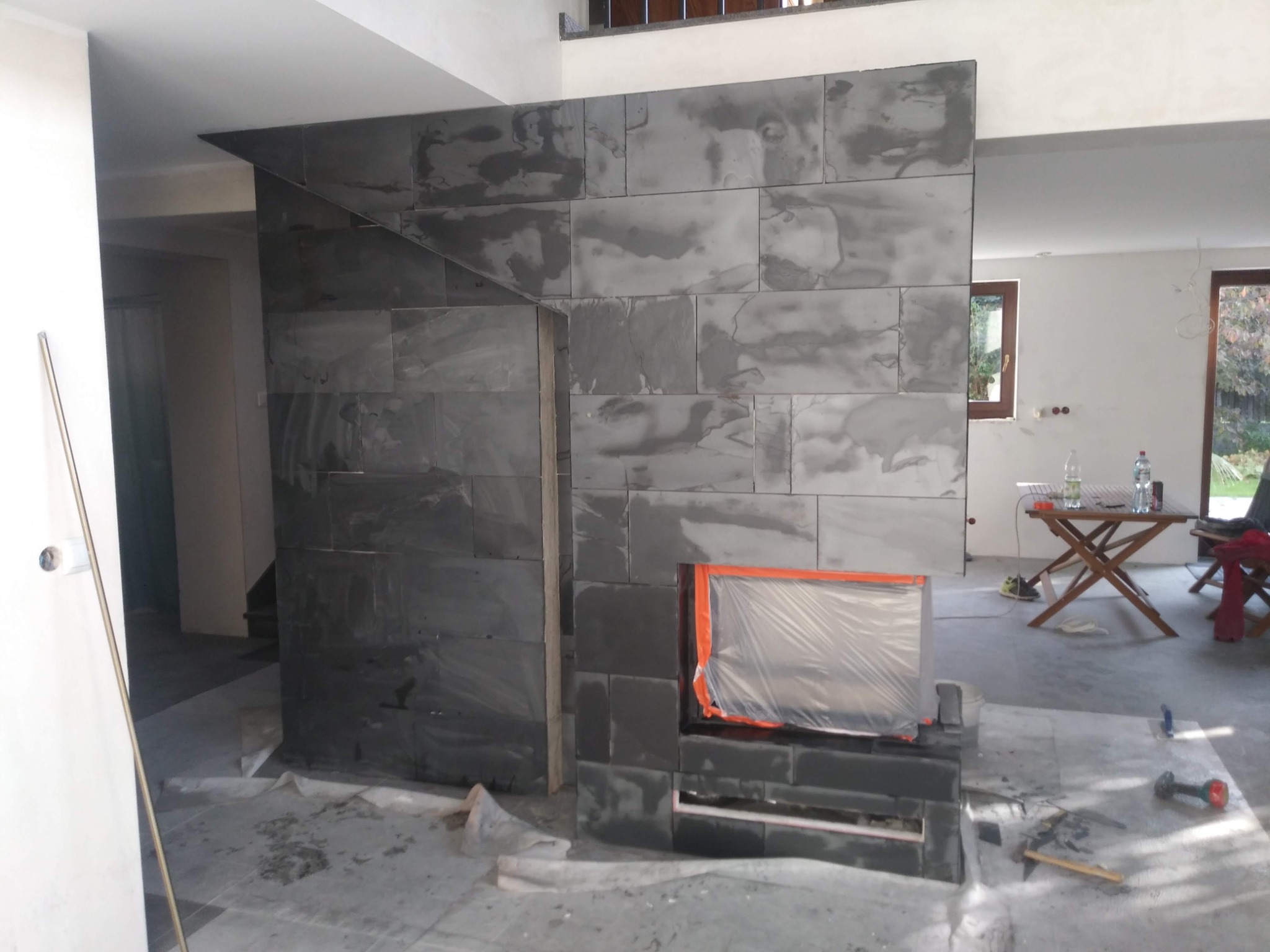 Montaż ściany działowej z płytek imitujących kamień w surowym wnętrzu, widoczne narzędzia i zabezpieczony otwór na kominek.