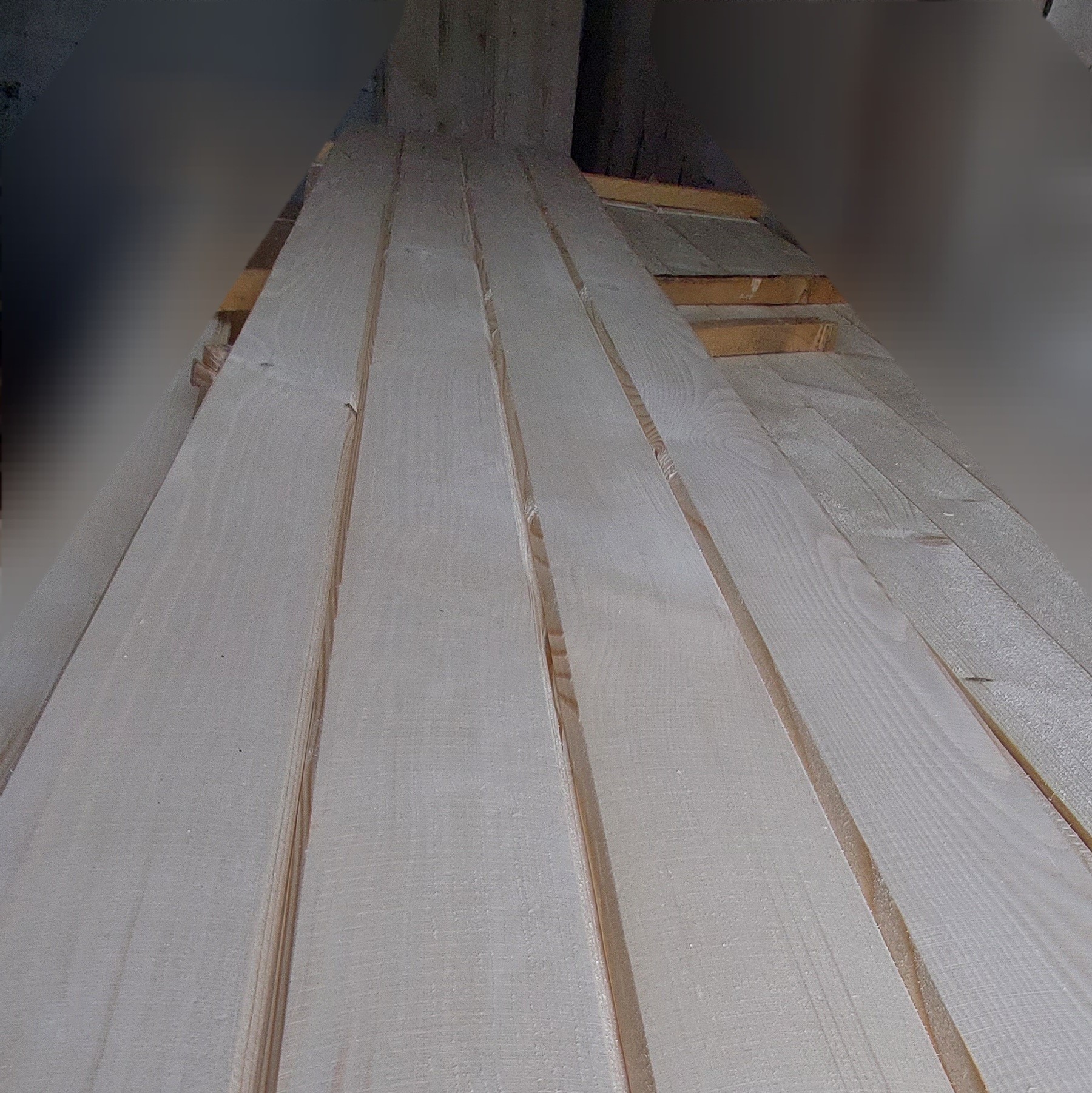 Stos świeżo oheblowanych desek z widocznymi słojami drewna, ułożonych warstwami w magazynie.