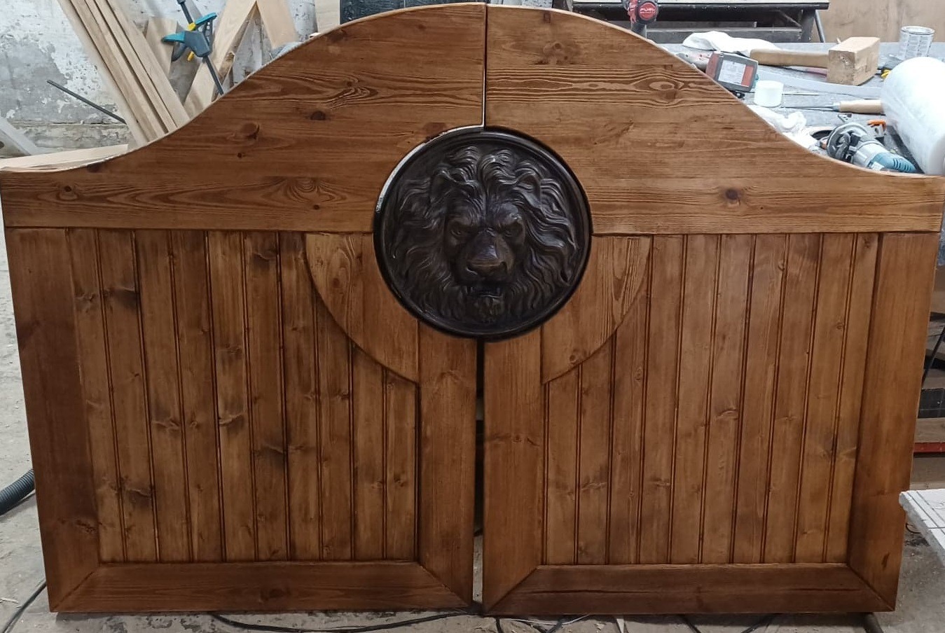 Rustykalne, dwuskrzydłowe, drewniane drzwi z ozdobnym, metalowym lwem pośrodku, widoczne w warsztacie stolarskim.