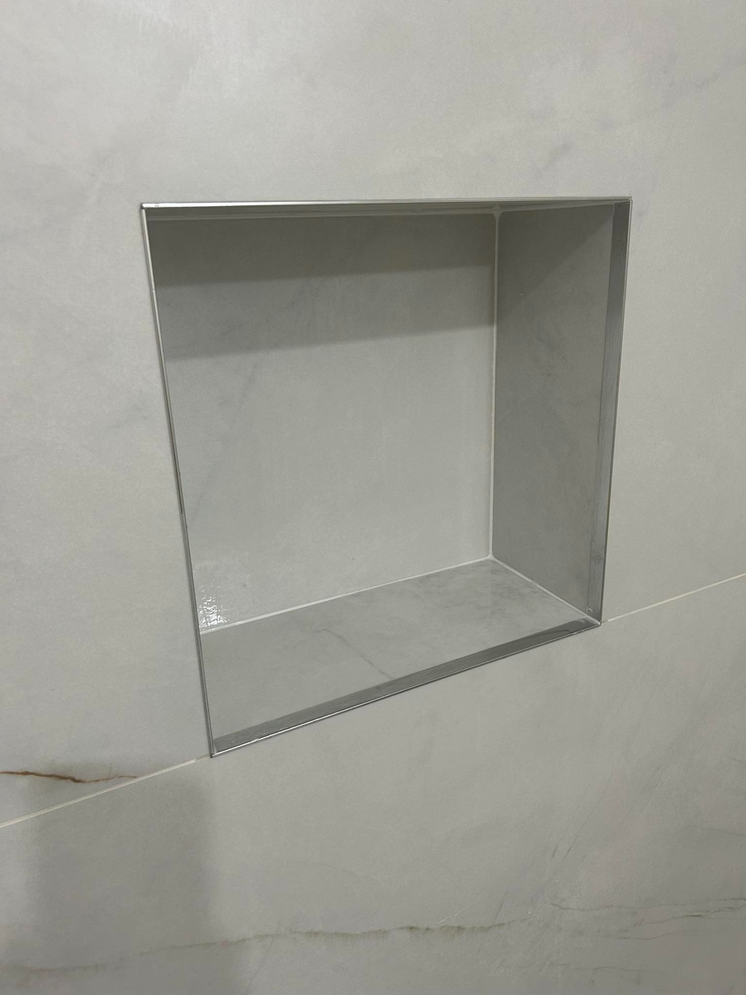 Wnęka w ścianie wyłożona szarą płytką z metalowym obramowaniem, widoczne delikatne żyłki na płytkach.