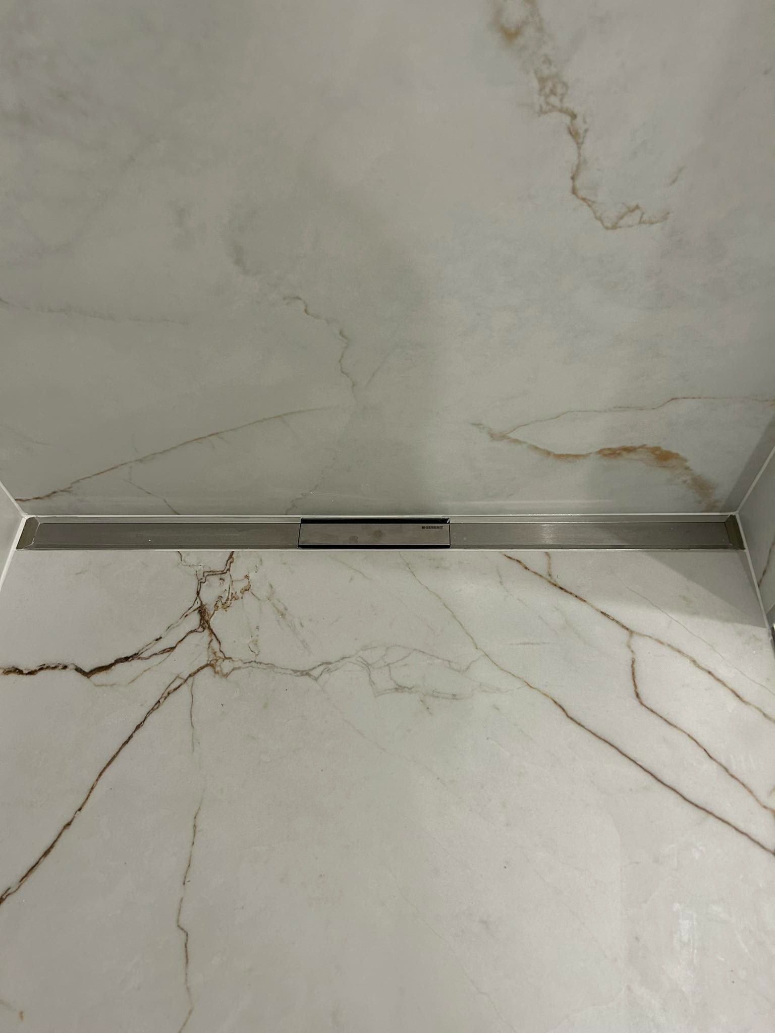 Wykończona łazienka z beżowymi marmurkowymi płytkami i liniowym odpływem podłogowym Geberit.