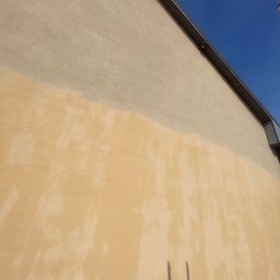 Bartosz Prelewski DomyjDach - Częściowo umyta, beżowa elewacja budynku z widocznym cieniem drabiny. Kontrast czystej i zabrudzonej powierzchni. Górna część elewacji jest jaśniejsza.