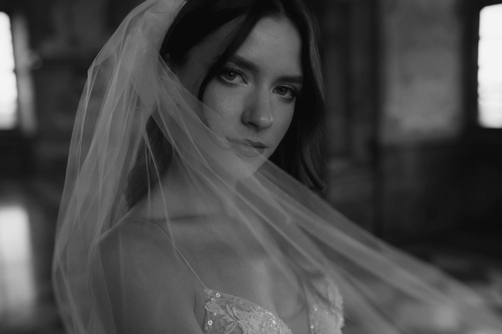 Portret kobiety w welonie, czarno-białe zdjęcie z delikatnym rozmyciem tła, ukazujące detale koronki na sukni.