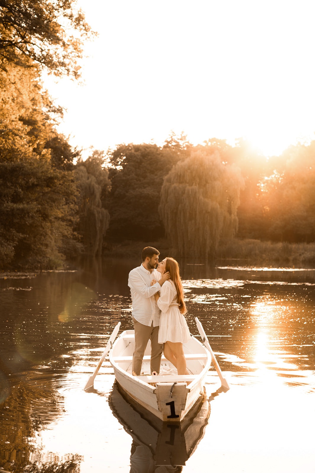 Zakochana para w łódce na jeziorze, w tle zachodzące słońce i drzewa.