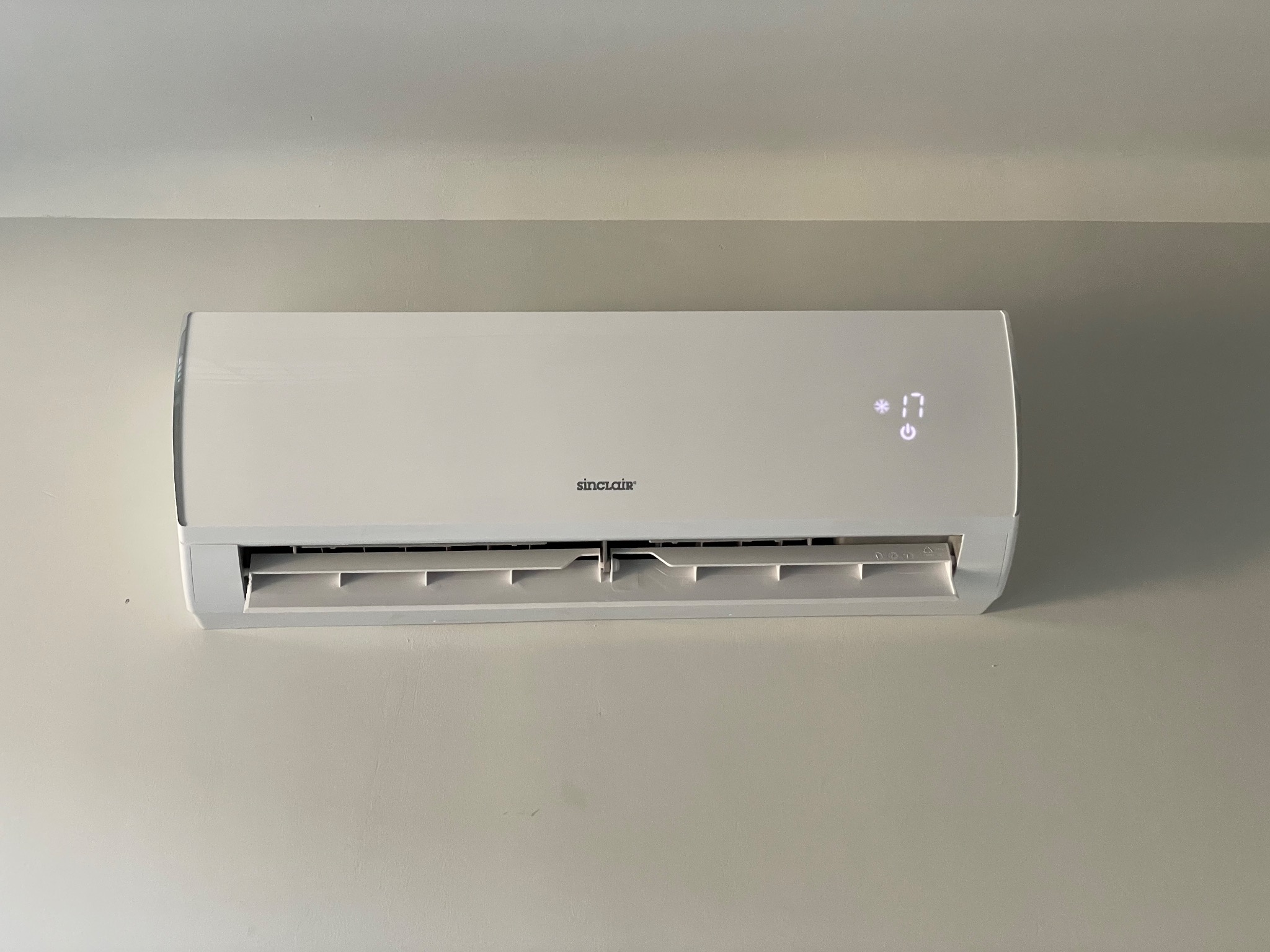 Biała jednostka wewnętrzna klimatyzacji Sinclair zamontowana na jasnej ścianie, z wyświetlaczem pokazującym temperaturę 17 stopni.