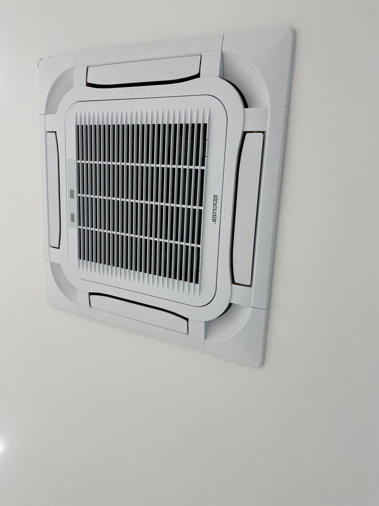 Biała, sufitowa jednostka klimatyzacji Sinclair zamontowana na białym suficie, widoczna z perspektywy lekko z dołu.