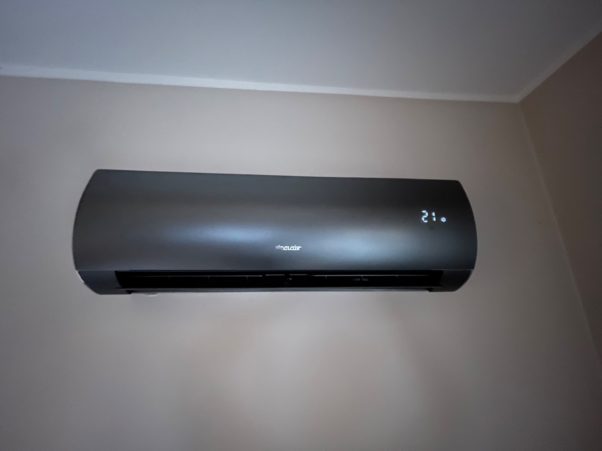 Czarny klimatyzator Sinclair zamontowany na jasnej ścianie, wyświetlający temperaturę 21 stopni Celsjusza.