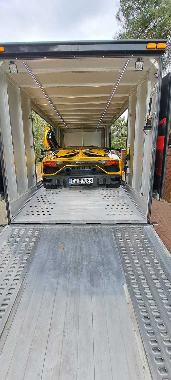 Żółty Lamborghini Aventador z otwartymi drzwiami, umieszczony wewnątrz aluminiowej lawety z oświetleniem LED, widok z tyłu, polska tablica rejestracyjna.