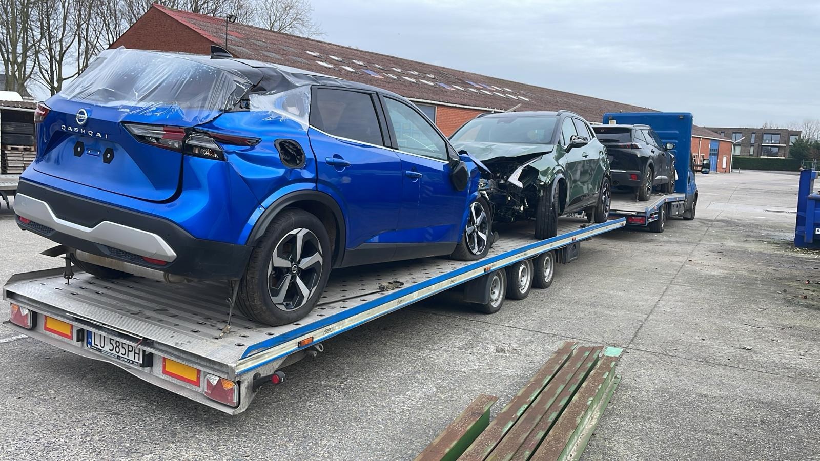 Niebieski Nissan Qashqai z uszkodzonym tyłem, owinięty folią, stoi na lawecie obok zielonego i czarnego uszkodzonego samochodu, widoczne tablice rejestracyjne LU 585PH.