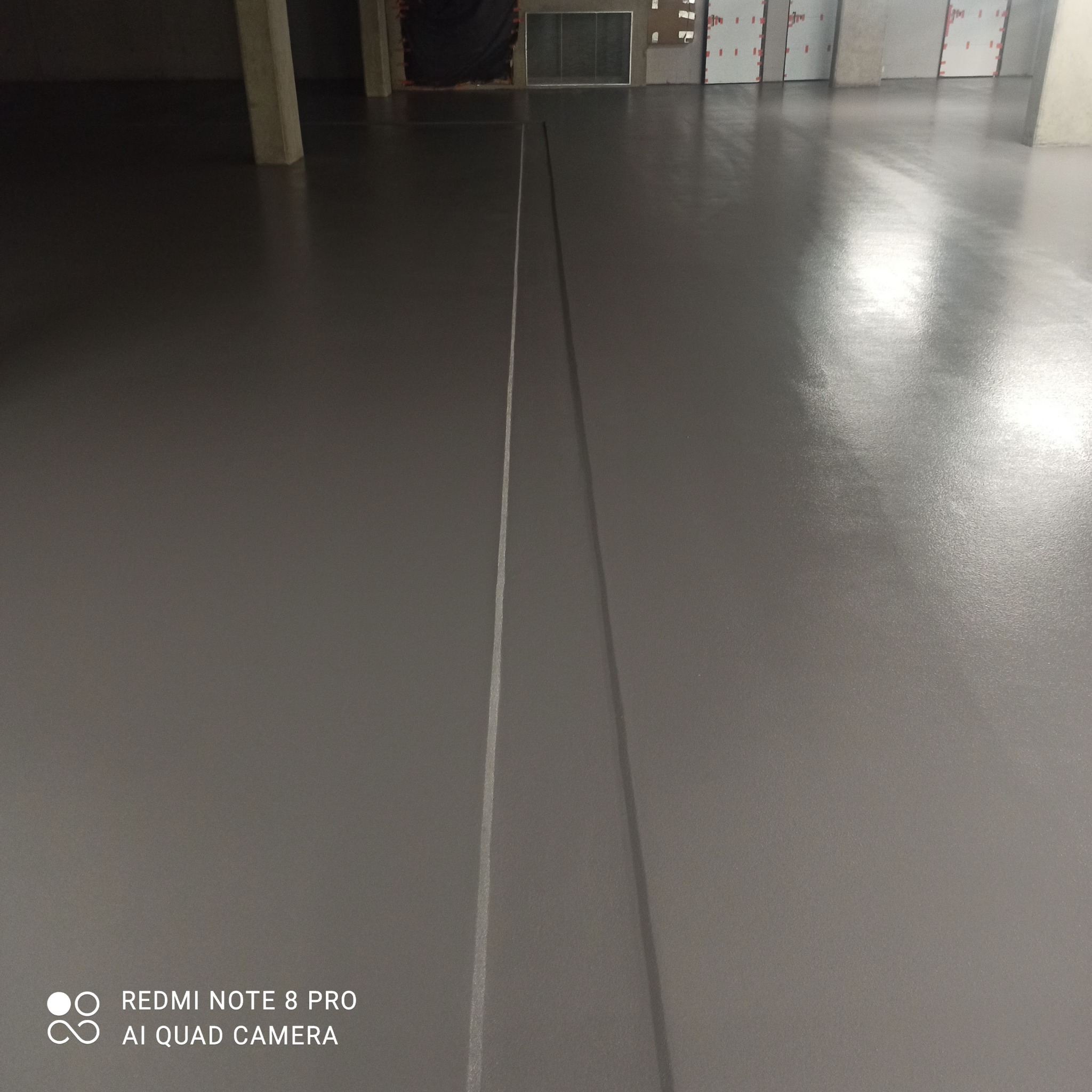 Gładka, szara posadzka w hali garażowej, z widocznymi dylatacjami i słupami konstrukcyjnymi w tle.