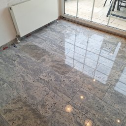 Patrex uslugi budowlane patryk rydz - Ułożona, polerowana podłoga z płytek imitujących kamień, z widocznymi plastikowymi krzyżykami dystansowymi, grzejnik ścienny i odbicie światła w oknie.