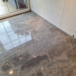 Patrex uslugi budowlane patryk rydz - Ułożona podłoga z płytek imitujących kamień, z widocznym odbiciem okna i roślinności, oraz fragmentem ściany z fakturą baranka.