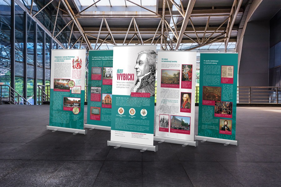 Zestaw roll-upów prezentujących informacje o Józefie Wybickim, w neutralnym wnętrzu z przeszklonymi ścianami i metalową konstrukcją dachu.